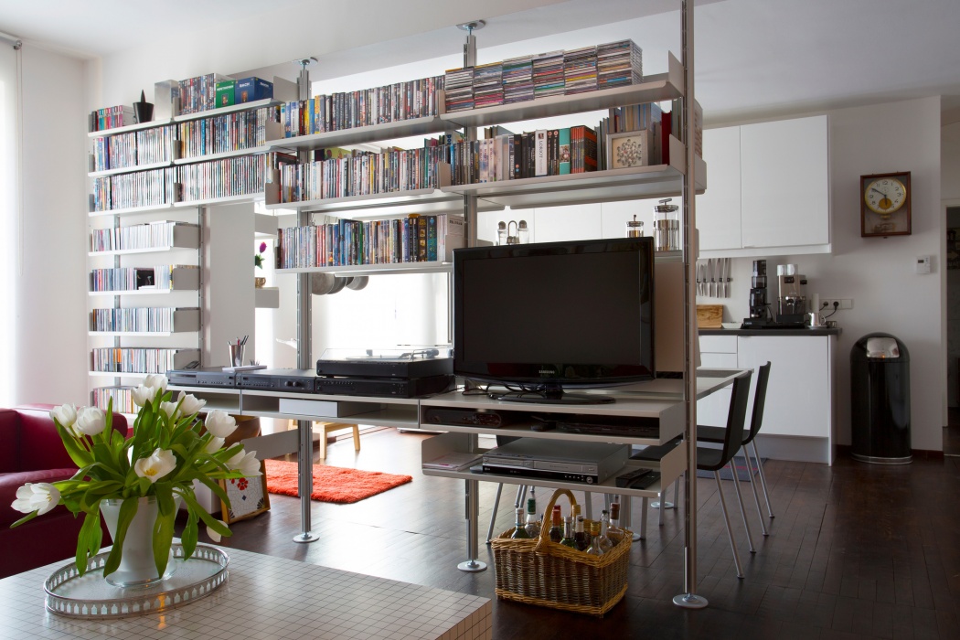 Wall mounted to the left; compressed between floor and ceiling on the right. Double shelves for remotes with Braun separates and record player above. CDs and DVDs all around. See the kitchen side of this system